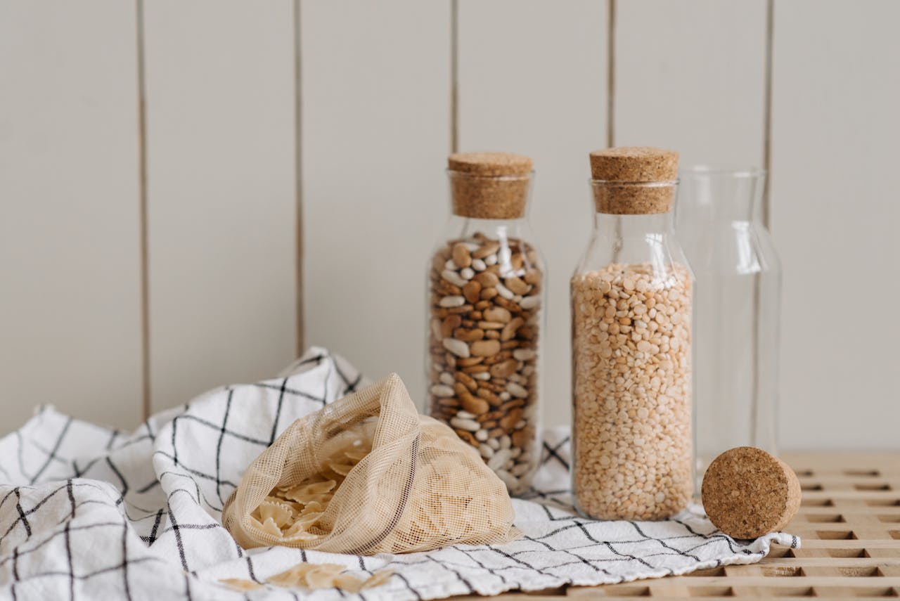 about-02 Eco-friendly jars filled with beans and grains, featuring a mesh bag and cloth on a wooden surface.